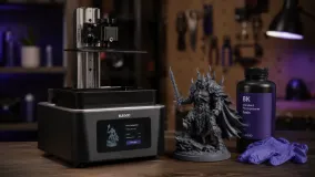 A resin 3D printer next to a highly detailed miniature it produced