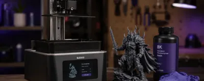 A resin 3D printer next to a highly detailed miniature it produced