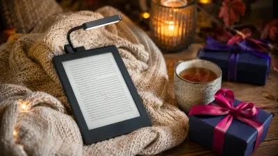 A cozy reading gift setup with an e-reader, a warm blanket, a book light, and a mug