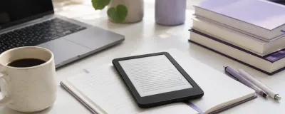 Kindle e-reader on a desk next to textbooks, notebooks, and a coffee cup in a student study setup