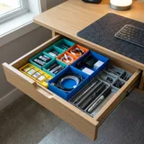 A desk drawer filled with colorful 3D printed Gridfinity modular storage bins holding tools and office supplies