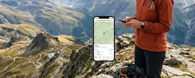 A traveler on a mountain summit checking offline map navigation on a smartphone next to an open backpack