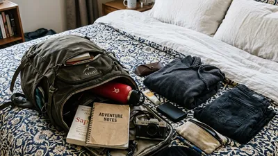 An open backpack with packing cubes and travel gear laid out on a bed