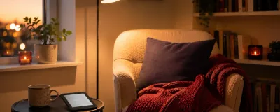 A cozy reading nook with a comfy chair, warm lamp, blanket, and a small shelf of books
