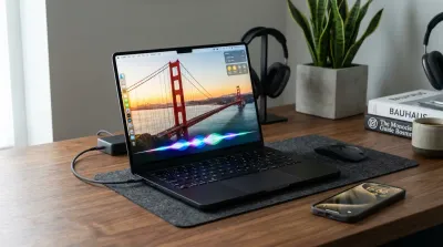 A Space Black MacBook Pro running macOS Golden Gate and an iPhone with glowing Siri AI waveforms on a wooden desk.