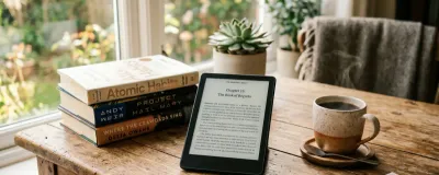Kindle e-reader on a desk with a book and a cup of coffee