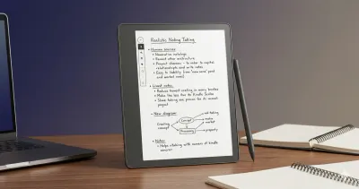 Kindle Scribe on an office desk with handwritten meeting notes on screen next to a laptop.