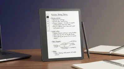 Kindle Scribe on an office desk with handwritten meeting notes on screen next to a laptop.