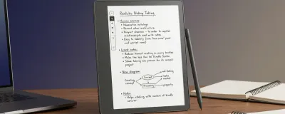 Kindle Scribe on an office desk with handwritten meeting notes on screen next to a laptop.
