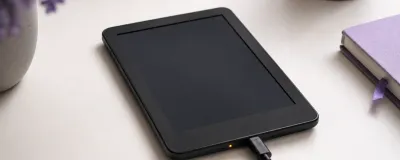 A black Kindle e-reader lying face up with a blank, unresponsive screen next to a USB-C charging cable