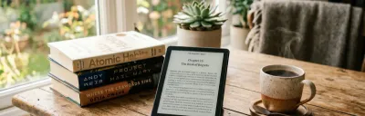 Kindle e-reader on a desk with a book and a cup of coffee