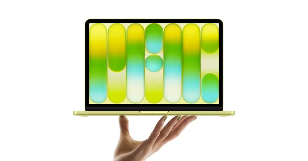 A sleek Indigo MacBook Neo on a wooden desk with coffee and 3D printed accessories.