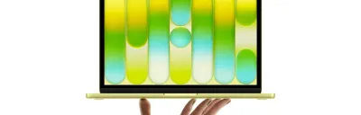 A sleek Indigo MacBook Neo on a wooden desk with coffee and 3D printed accessories.